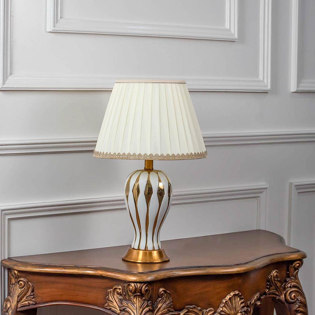 White ceramic table lamp turned off with pleated lampshade and gold striped detailing displayed on white background decor.