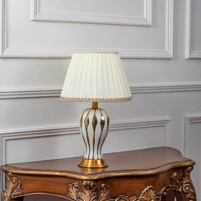 White ceramic table lamp turned off with pleated lampshade and gold striped detailing displayed on white background decor.