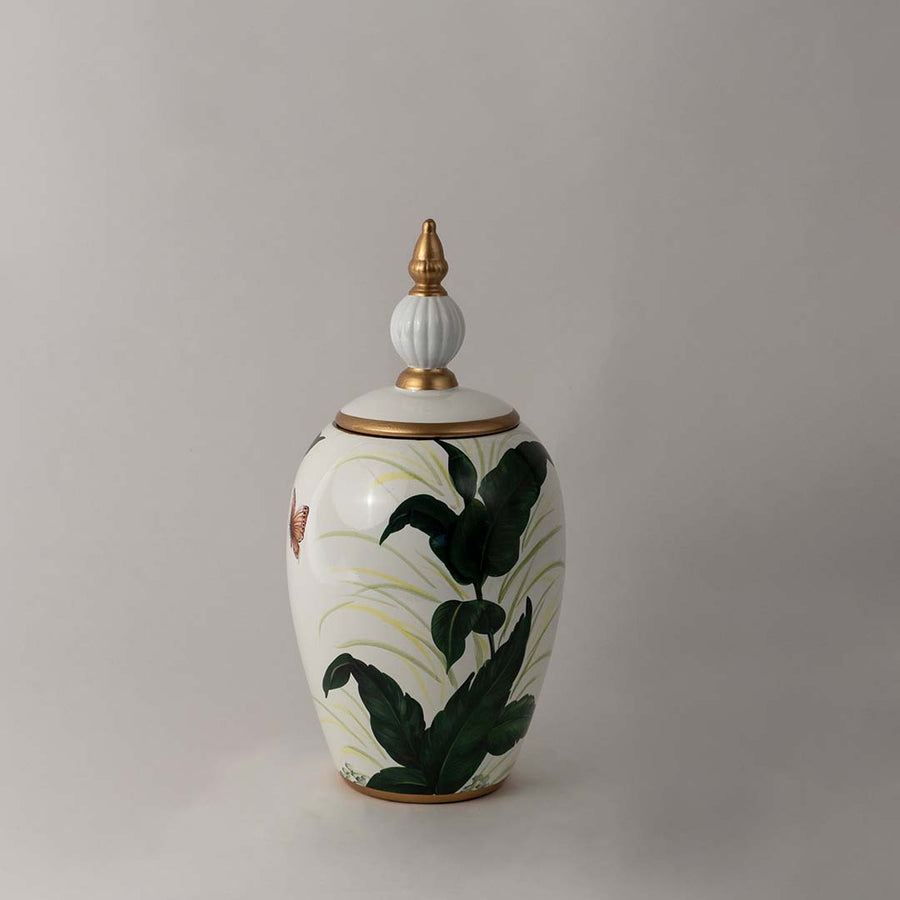 Decorative ceramic jar with green botanical leaf artwork and gold lid placed on white surface against neutral background showcasing elegant modern home decor styling.