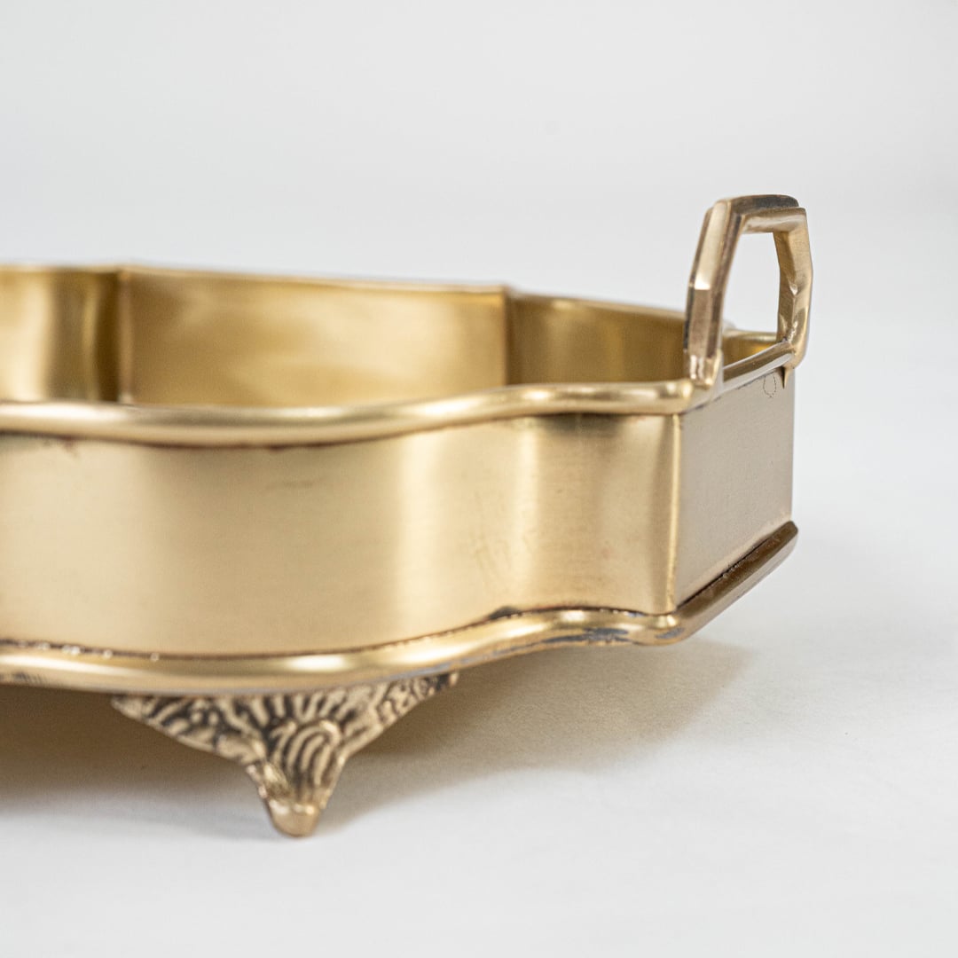 A closeup view of the ornate golden serving tray showing its intricate carved border smooth surface and elevated feet that enhance its premium handcrafted appearance.