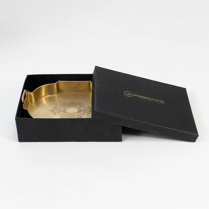 Brass serving tray with floral design partially packed in black premium gift box with golden logo on white base.