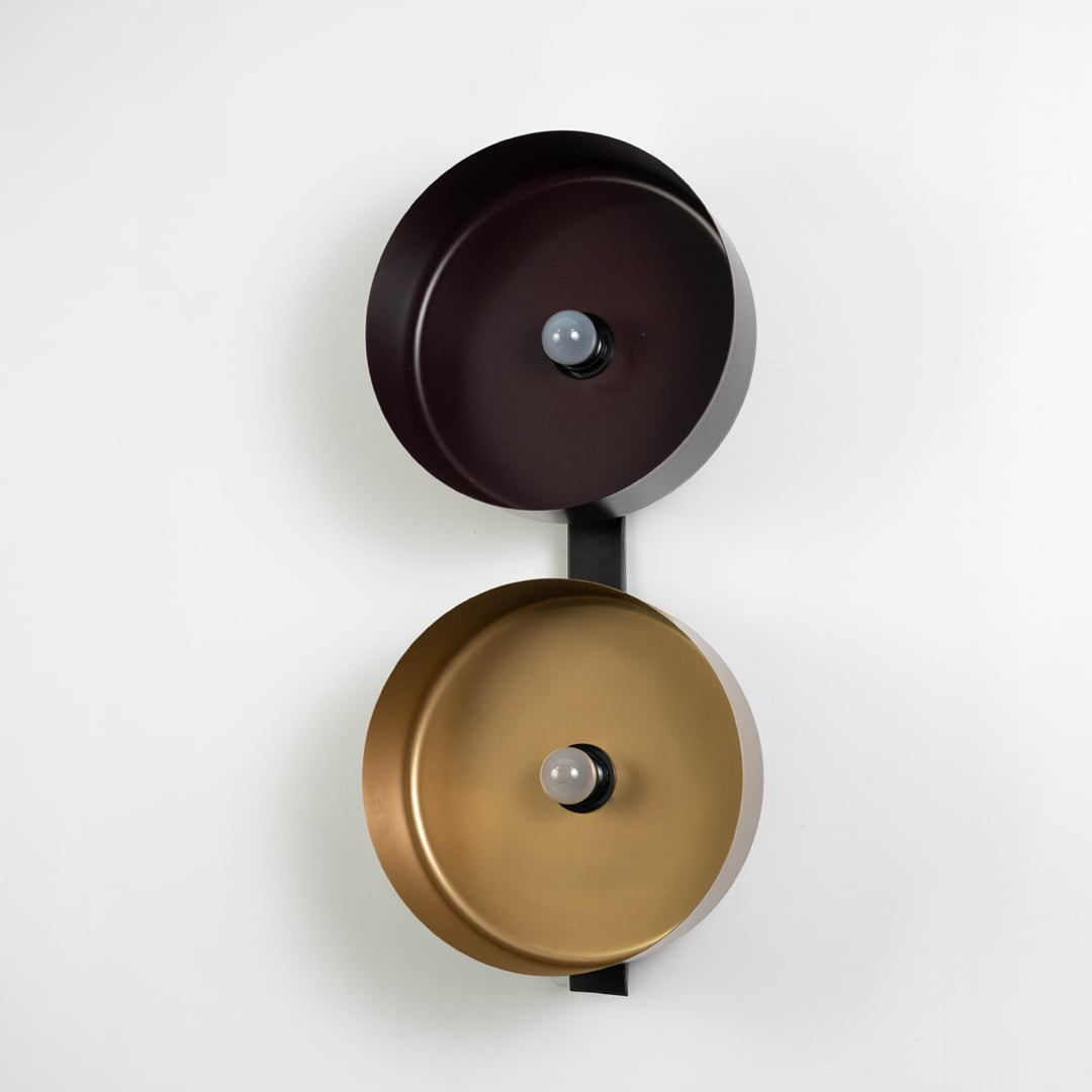 Bronze and gold reflector wall light mounted vertically on matte black base against clean white backdrop.
