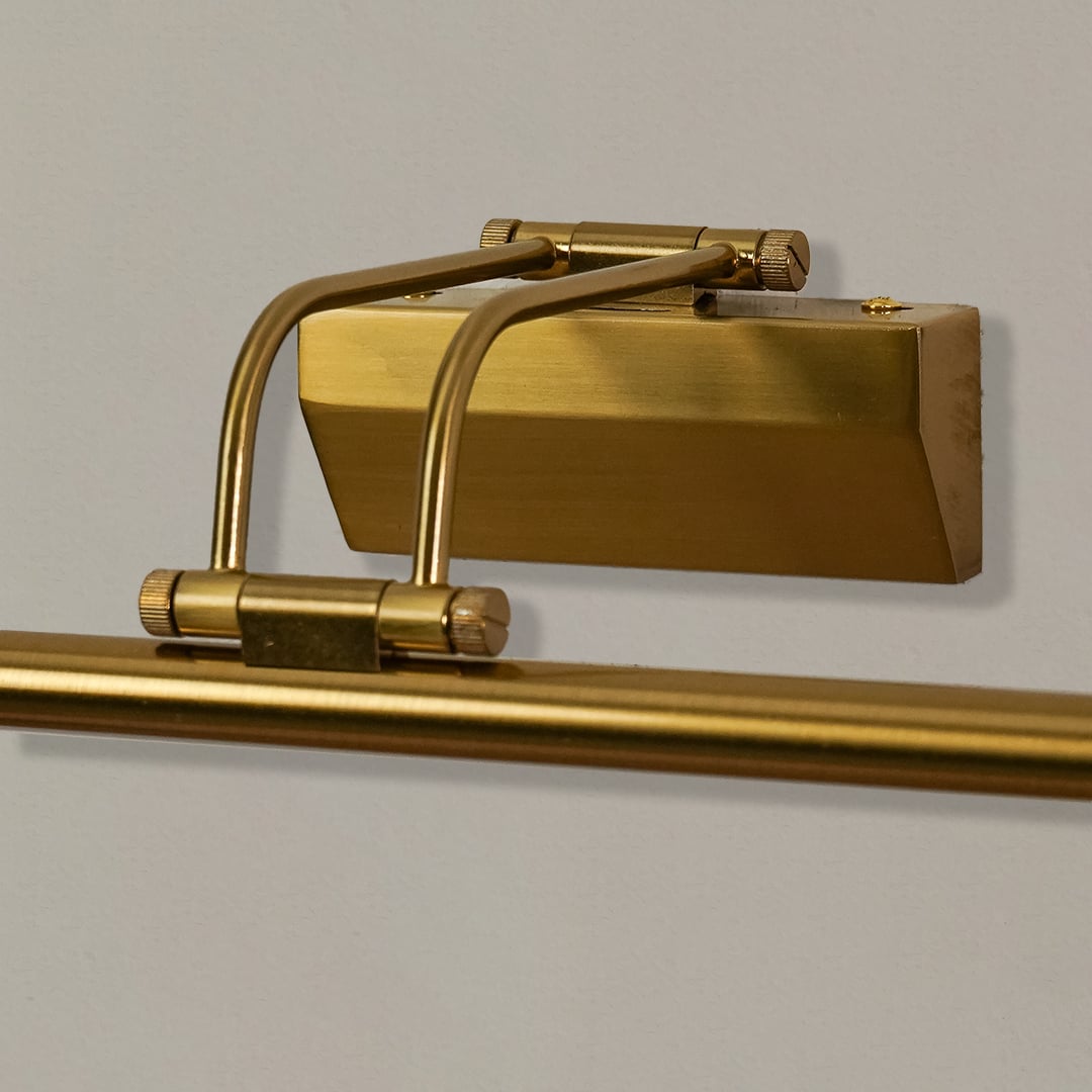 Closeup of gold metal picture light showing polished finish slim bar design and warm directional illumination.