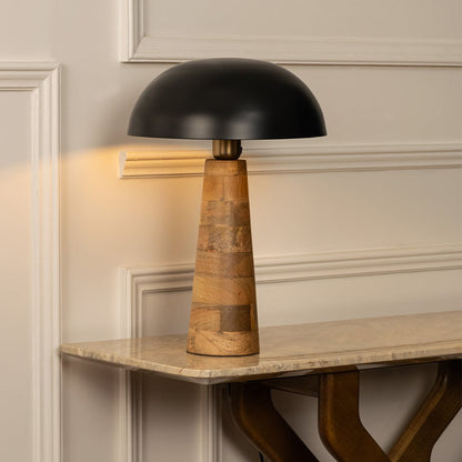 Black dome shade wooden cone table lamp on marble shelf with light on for artistic modern décor.