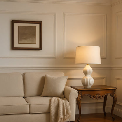 White ceramic table lamp placed beside a beige sofa on a wooden side table in a cozy living room setting casting warm ambient light that enhances modern and minimalist home decor.
