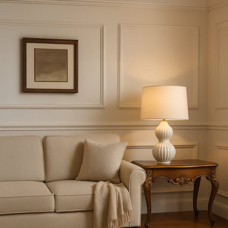White ceramic table lamp placed beside a beige sofa on a wooden side table in a cozy living room setting casting warm ambient light that enhances modern and minimalist home decor.