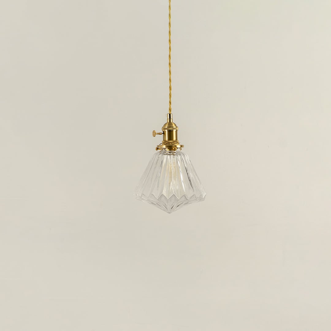 Unlit clear glass pendant light with golden brass holder hanging on yellow cord for sophisticated home decor appeal.