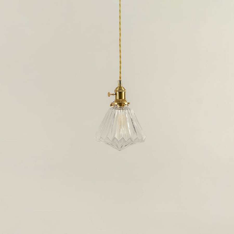 Unlit clear glass pendant light with golden brass holder hanging on yellow cord for sophisticated home decor appeal.