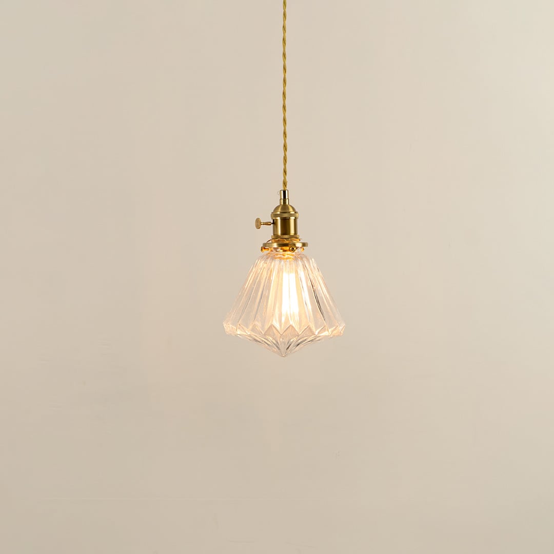 Clear glass pendant light with brass holder glowing softly on white background for elegant living room lighting.