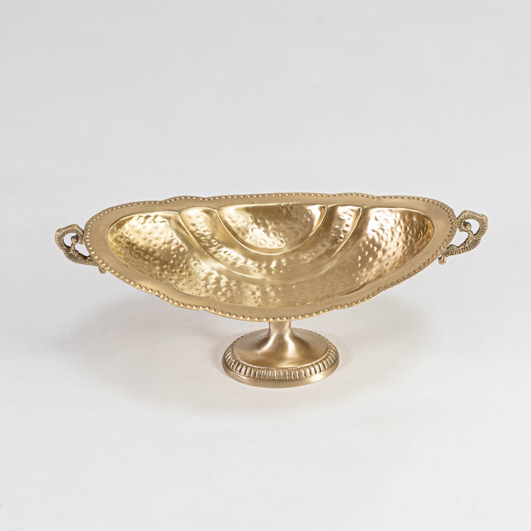 Closeup of hammered gold metal fruit bowl with dotted rim detailing and matte interior finish shown on white base.
