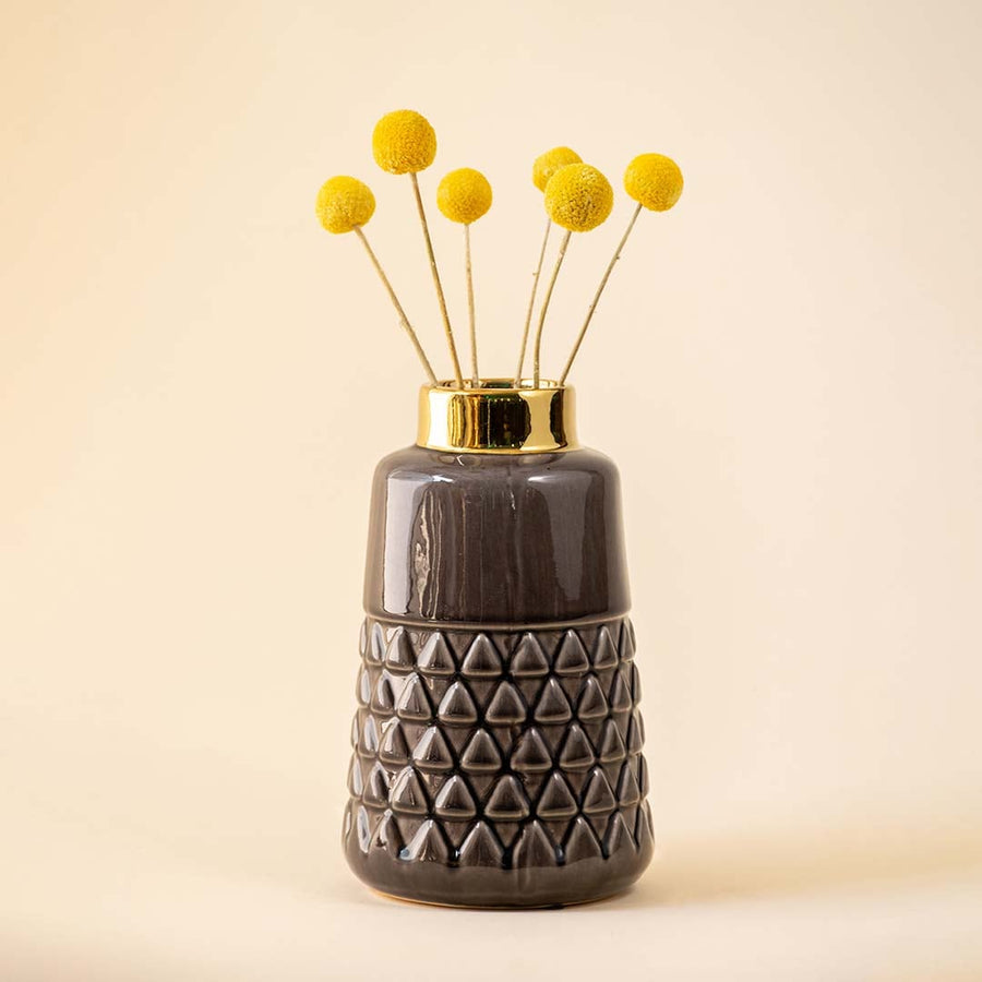 A stylish ceramic vase with a golden top holding yellow floral stems placed in a neutral toned interior setup adding a warm decorative touch to the room atmosphere.