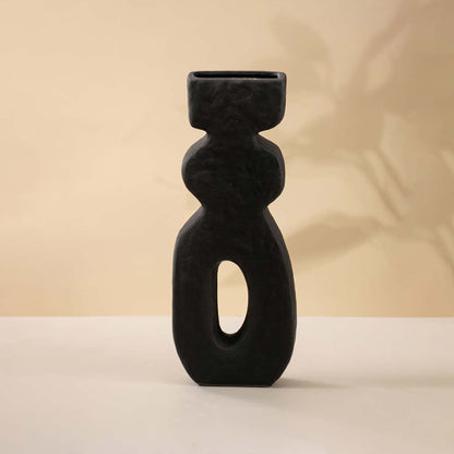 Minimalist black sculptural ceramic vase showcasing an elegant elongated structure with an artistic hollow form against white background.