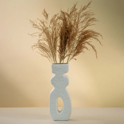White sculptural ceramic vase with tall modern silhouette and hollow center styled with dried pampas grass.