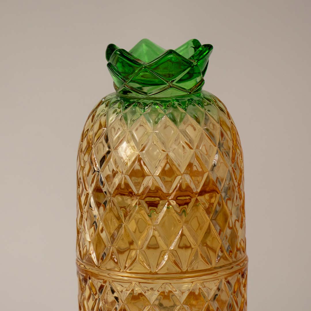 Closeup of pineapple shaped amber glass tumbler with detailed diamond texture and green crown lid for modern dining.