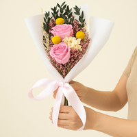 Hands holding a pink rose and yellow billy buttons dried floral bouquet wrapped with a pink ribbon for romantic gifting.