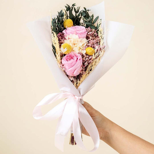 Preserved pink rose flower bouquet with white hydrangea yellow billy button and greenery on plain white background is a decorative gift bouquet.