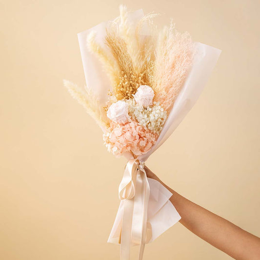 Hand holding a pastel pink and cream dried flower bouquet with cotton pods and pampas grass for minimalist rustic gifting.