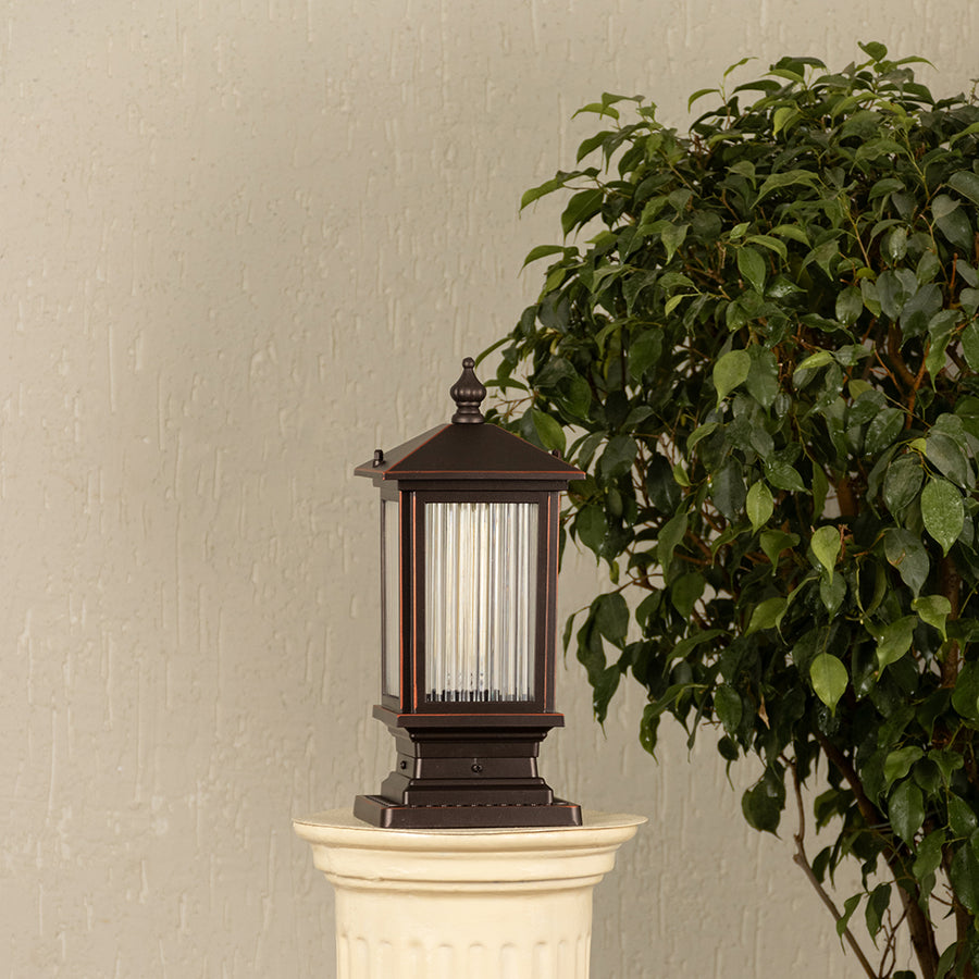 Black metal lantern with ribbed glass Light On placed next to a large green plant Lifestyle image for patio decor.