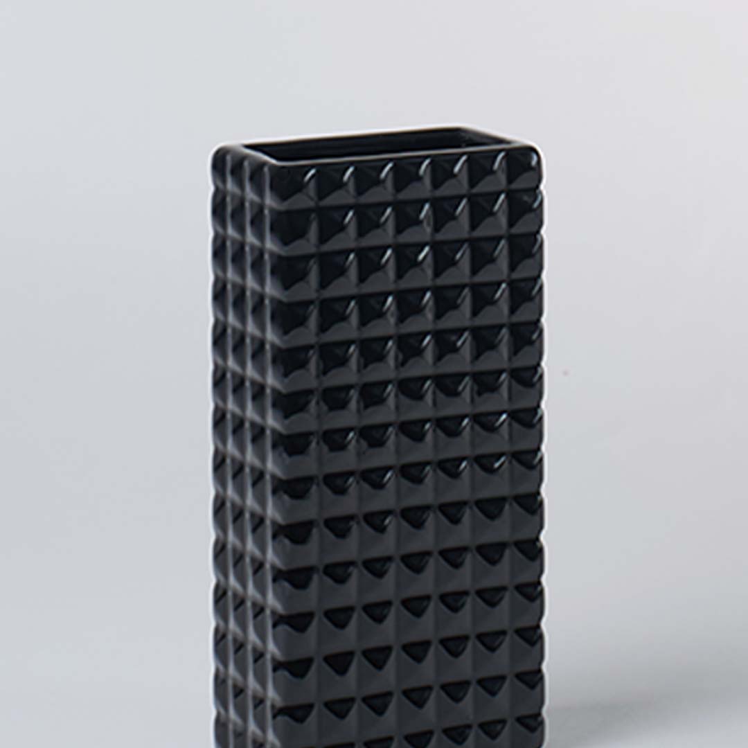 Closeup image of tall black ceramic vase with geometric textured surface highlighting bold form modern design and decor appeal.