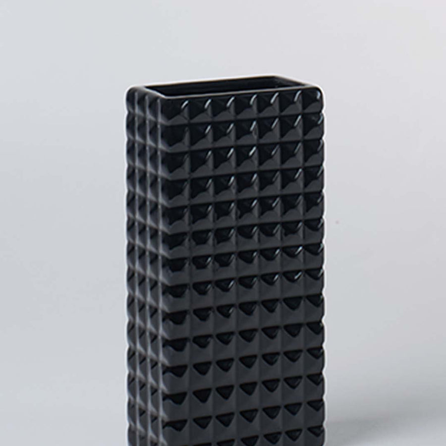 Closeup image of tall black ceramic vase with geometric textured surface highlighting bold form modern design and decor appeal.