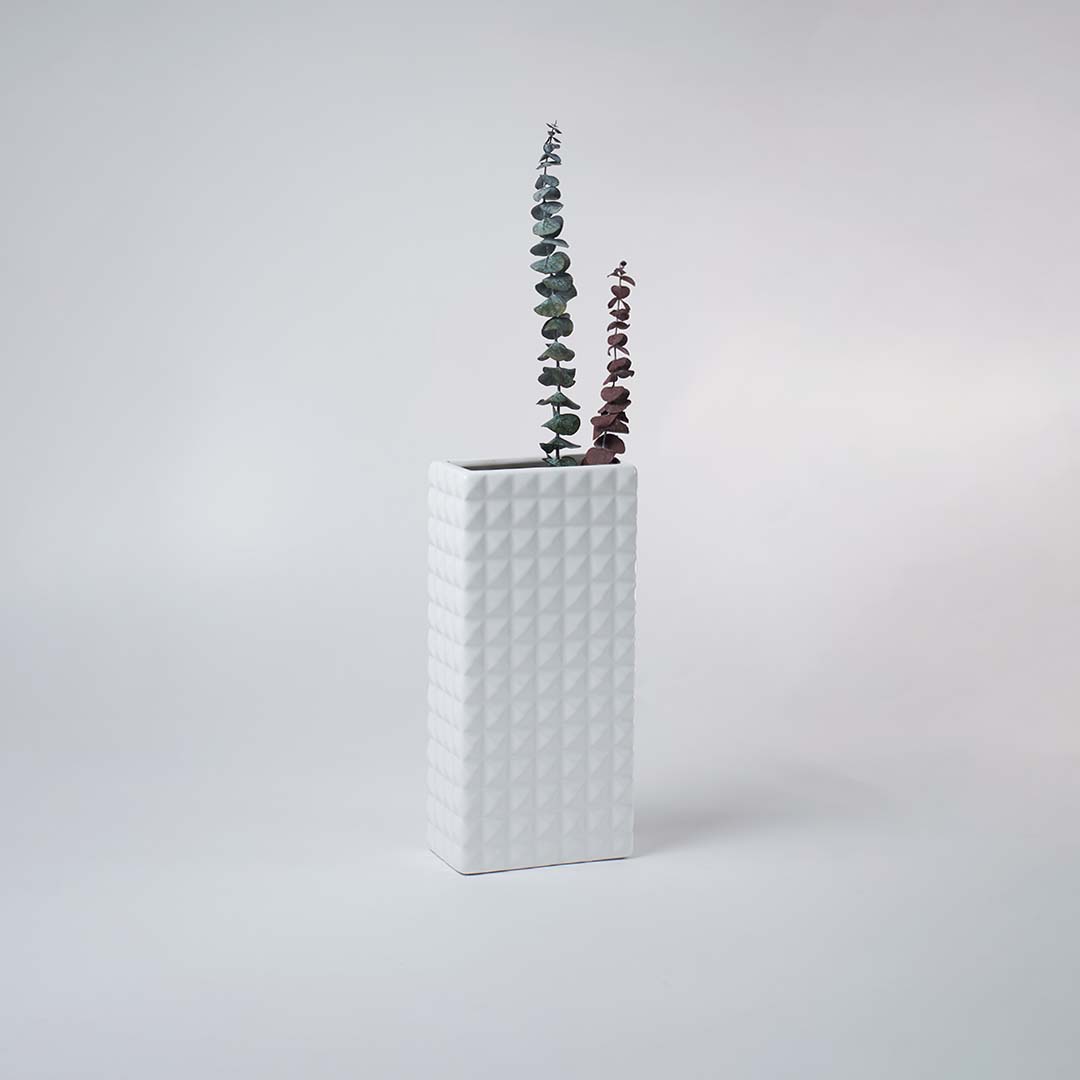 Minimal white ceramic vase with geometric texture placed on a soft background creating a clean contemporary decorative accent.