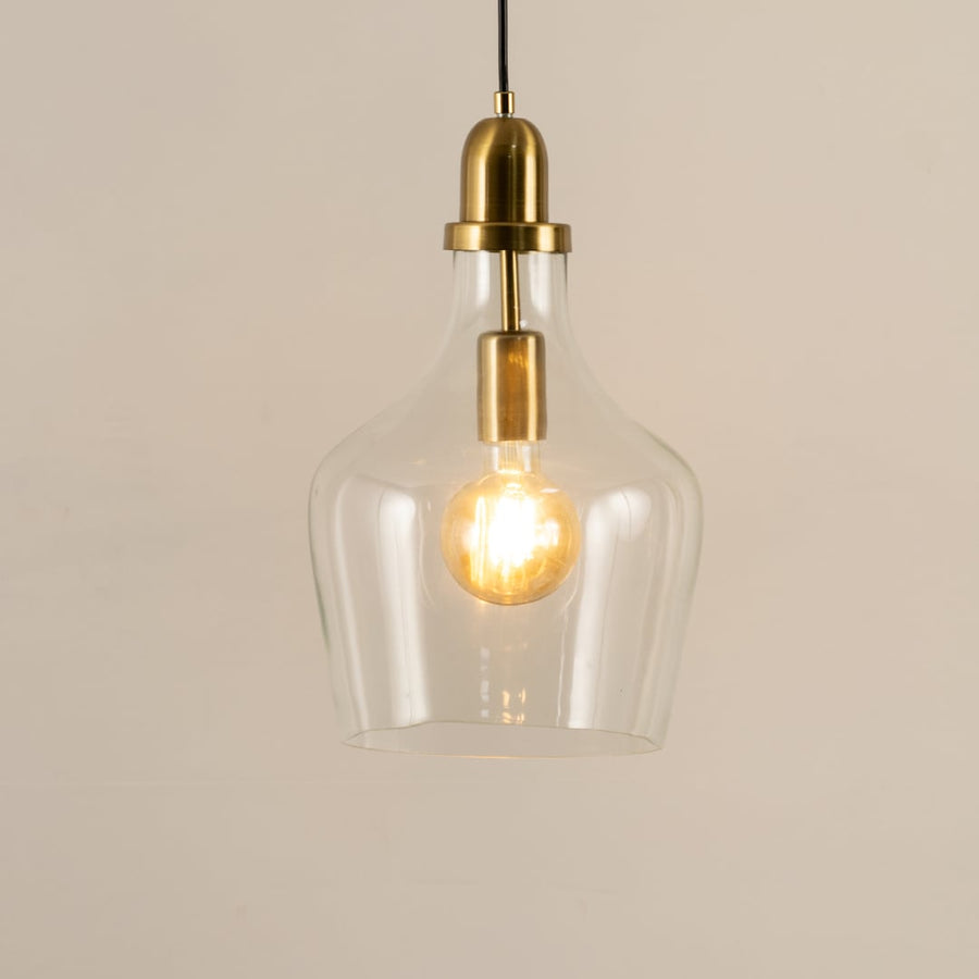 Clear glass and brass metal pendant light with exposed bulb adding warmth to stylish interiors.