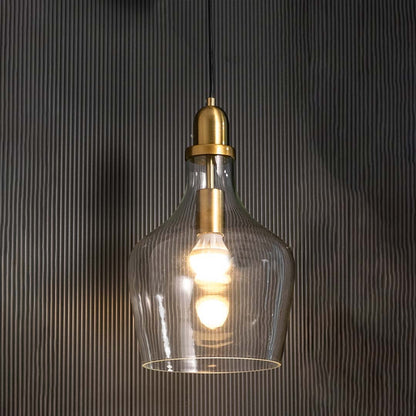 Pendant light with transparent glass shade lit warmly against a dark background emphasizing its golden holder and curved silhouette.