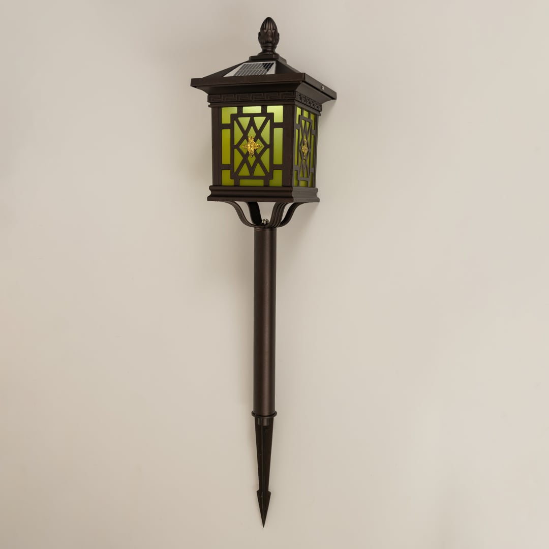 Brown solar spike lantern with patterned glass shown with light off on a white background highlighting its decorative detailing and outdoor ready structure.