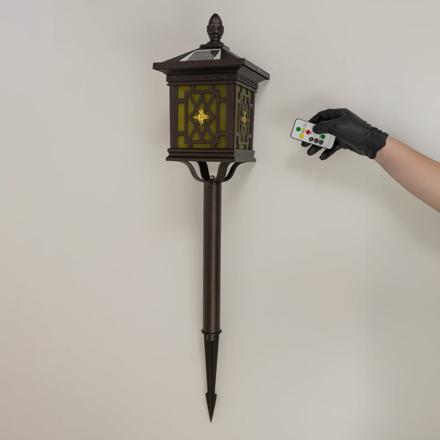 Brown solar garden spike lantern with patterned glass shown with light off on a white background showcasing its elegant frame and tall spike structure.