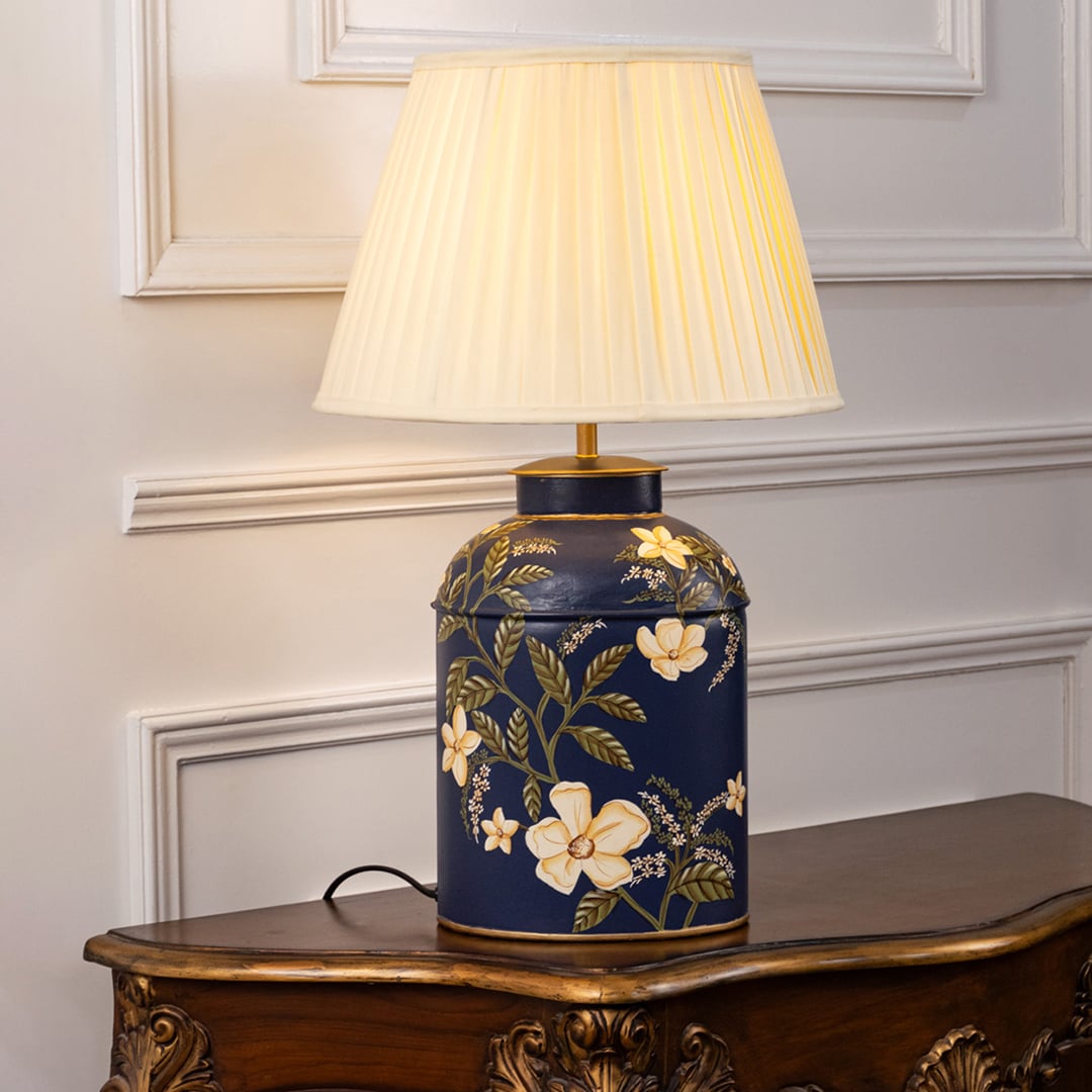 Table lamp on white background displaying ornate ceramic base with floral design and pleated shade for sophisticated ambient lighting.