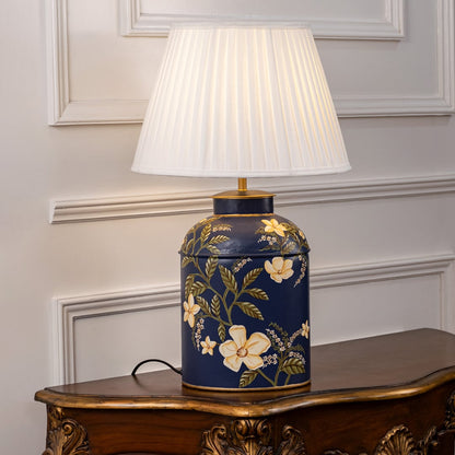 Table lamp on white background displaying ornate dark ceramic base with floral detailing and pleated shade for luxurious lighting appeal.