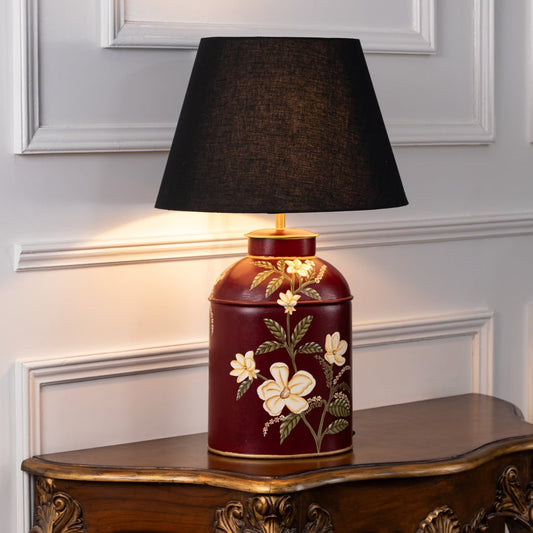 Table lamp on white background featuring deep red ceramic base with hand painted floral artwork and a black fabric lampshade.