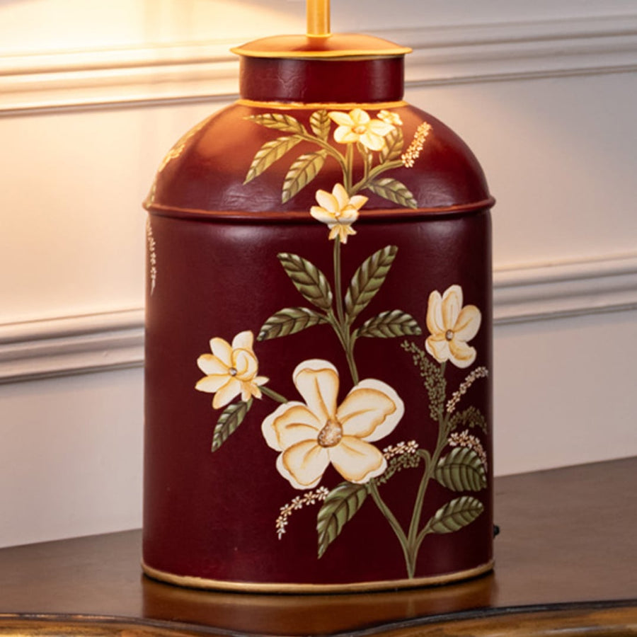 Table lamp closeup showing a deep red ceramic base with hand painted floral detailing and smooth glossy finish.