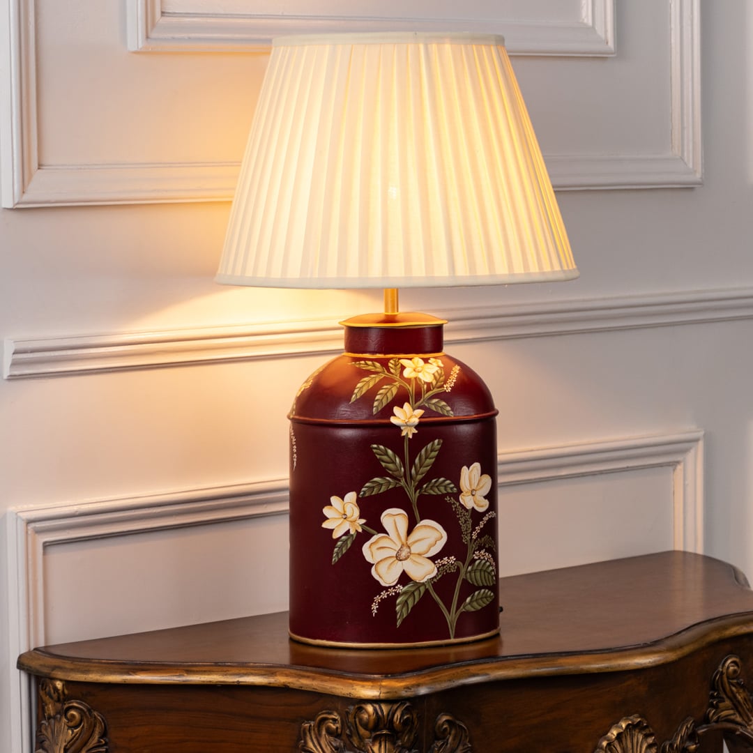 Table lamp on white background featuring a deep red ceramic base with elegant floral artwork paired with a soft pleated fabric lampshade.
