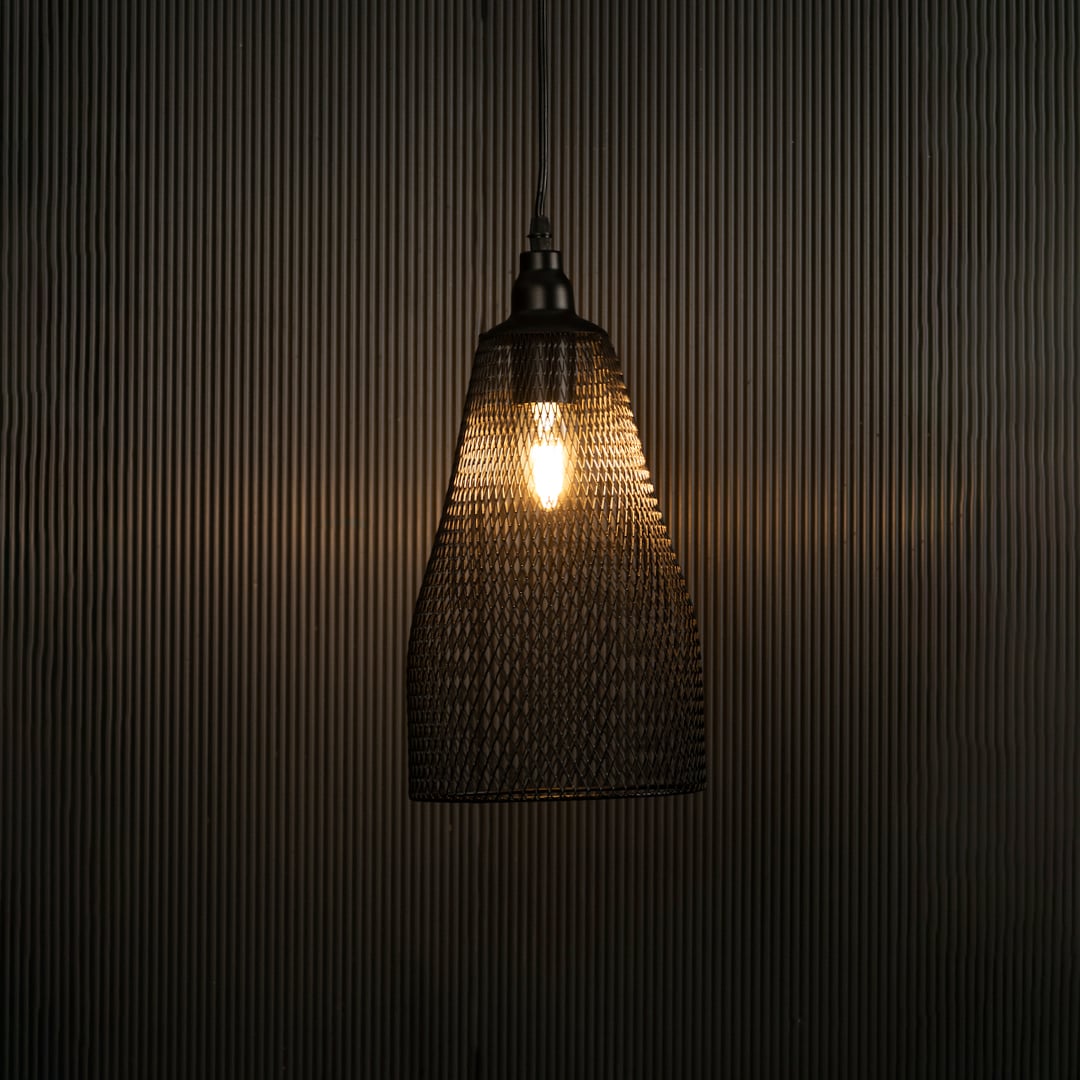 Elegant black mesh pendant hanging light illuminated against dark background highlighting its refined craftsmanship and industrial texture.
