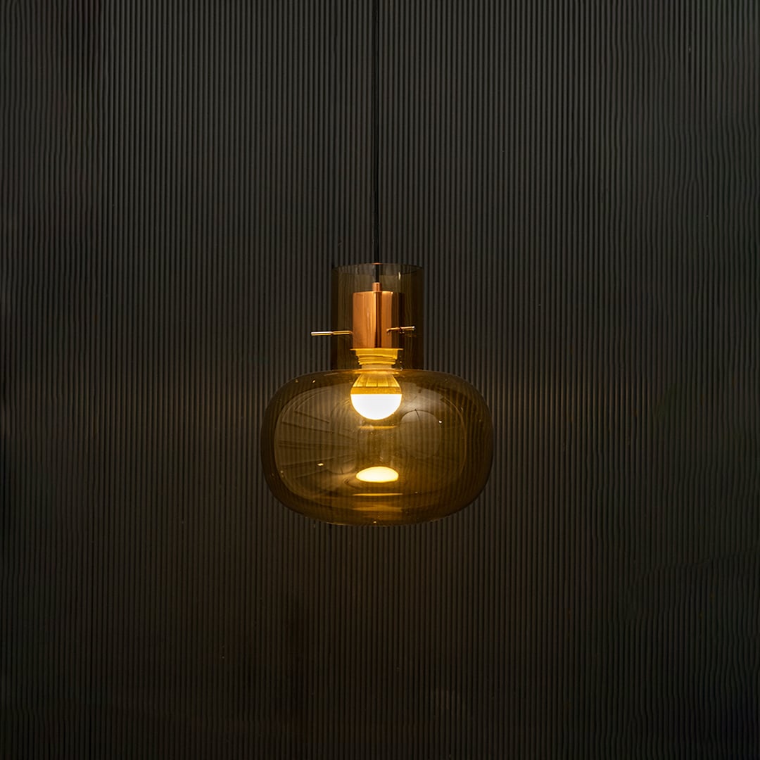 Amber glass ceiling pendant light illuminated beautifully on dark background highlighting elegant reflective texture.