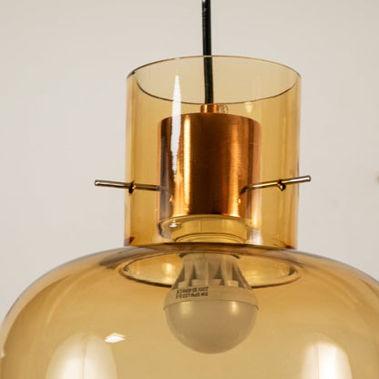 Close view of amber glass pendant light showing glossy surface golden top and bulb inside elegant craftsmanship.
