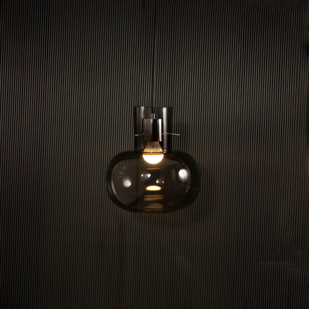Smoked glass wall light glowing on black background with warm filament bulb creating moody modern accent lighting for interior walls.