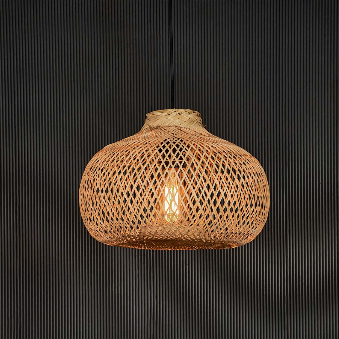 Woven rattan pendant light illuminated against black background highlighting its natural tone and warm glow.