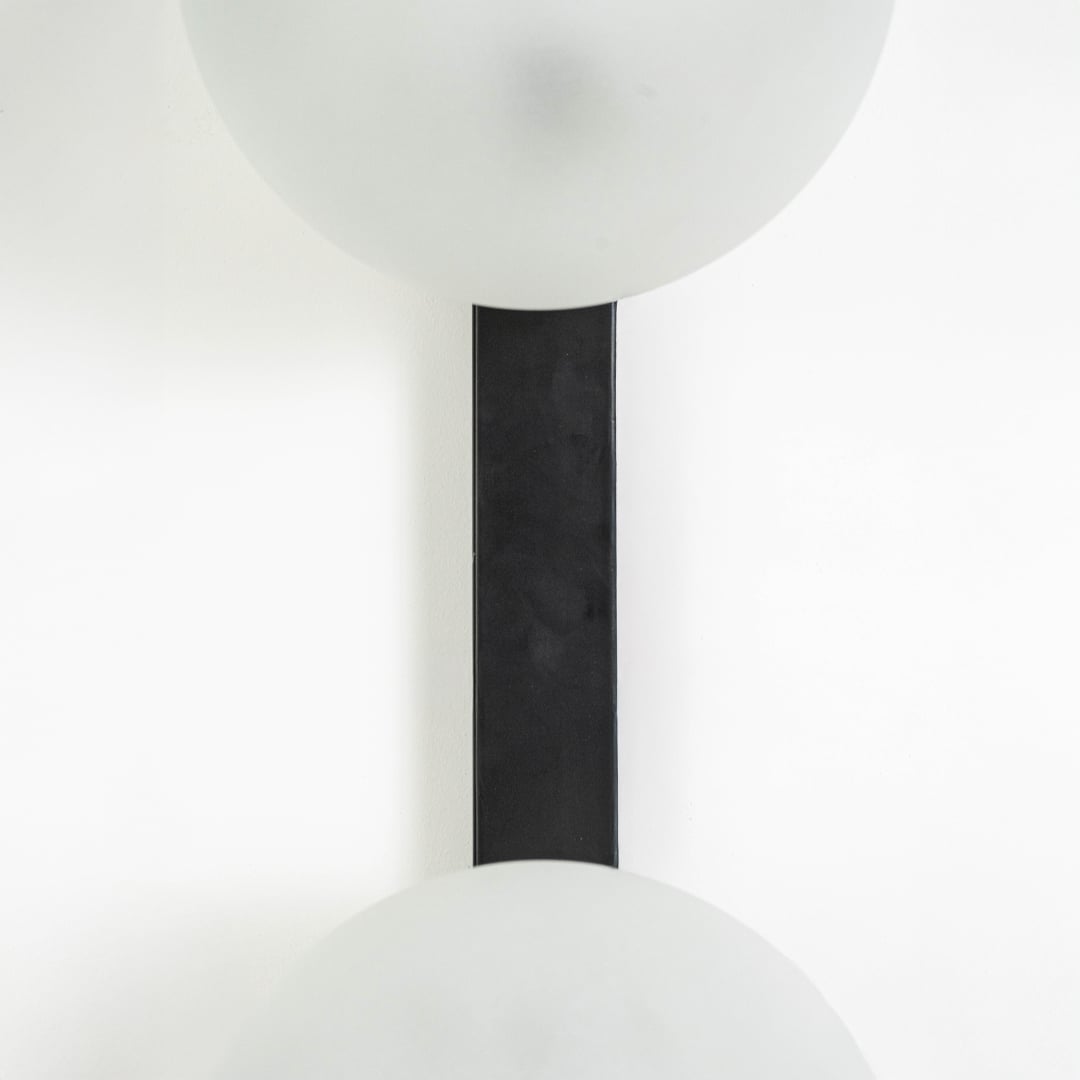 Vertical closeup of dual frosted glass wall lamp showing black metal support and seamless light placement.