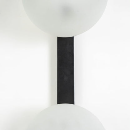 Vertical closeup of dual frosted glass wall lamp showing black metal support and seamless light placement.