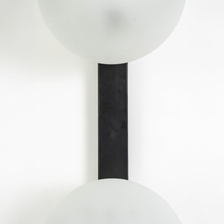 Vertical closeup of dual frosted glass wall lamp showing black metal support and seamless light placement.