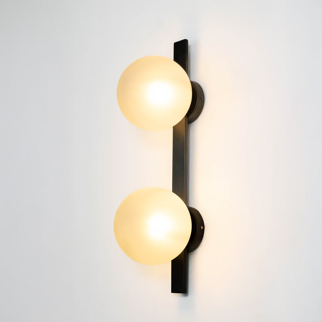 Modern wall light in black metal finish with dual globe glass shades for bedroom or living decor lighting white background.