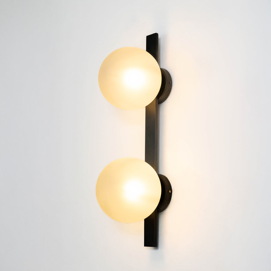Modern wall light in black metal finish with dual globe glass shades for bedroom or living decor lighting white background.