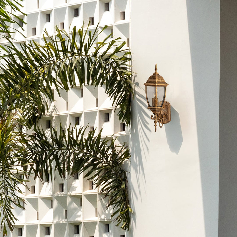 Vintage gold wall lantern styled against a minimal backdrop adding a warm classic touch to home exteriors with clear glass and a glowing bulb.