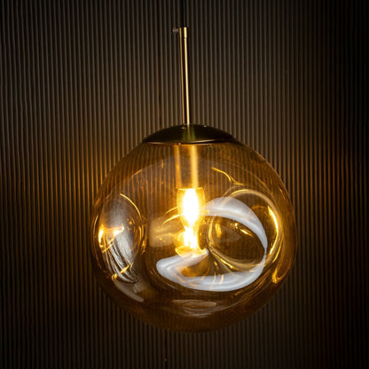 Amber glass globe pendant light glowing beautifully on black background creating warm and luxurious atmosphere.