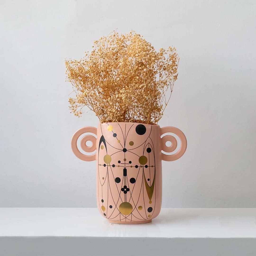 Golden dried gypsophila flowers arranged in decorative pink ceramic vase with artistic handles elegant lifestyle decor.