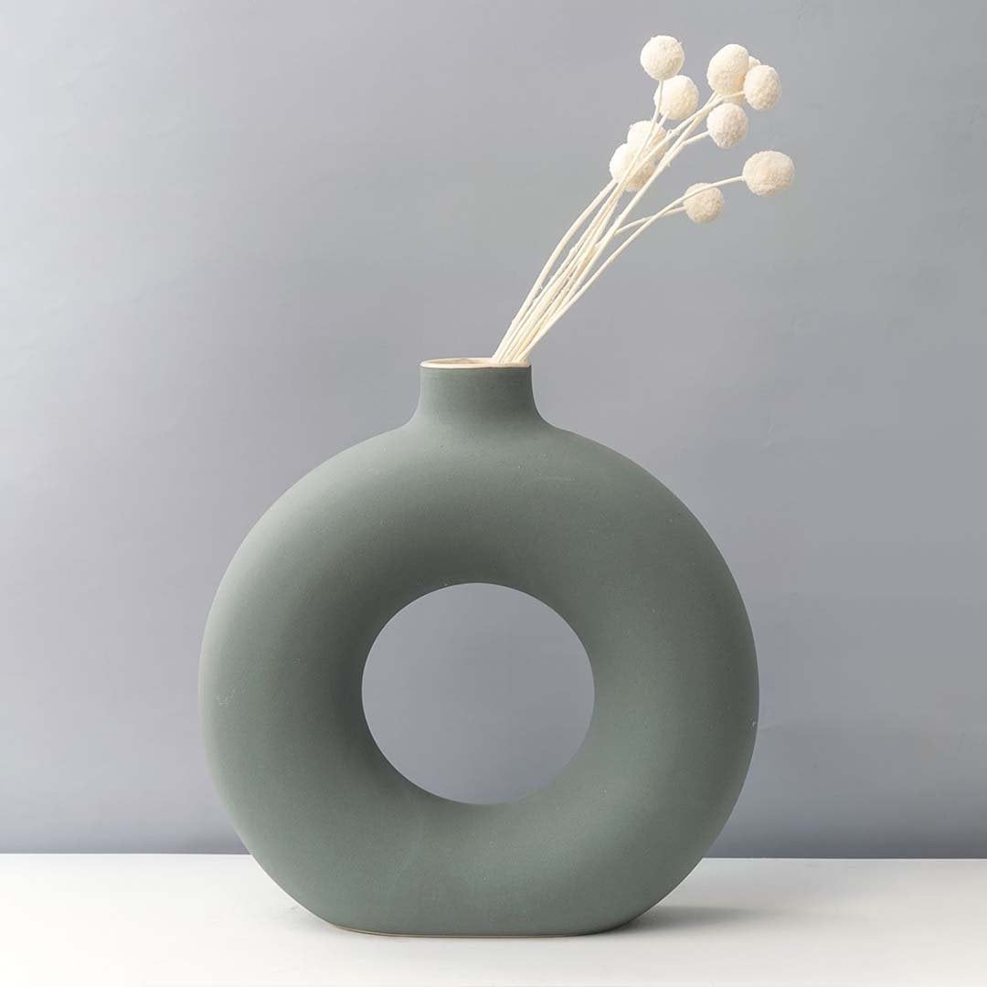 Grey round ceramic vase with hole design styled with white dried flower stems modern home decor accent for table.