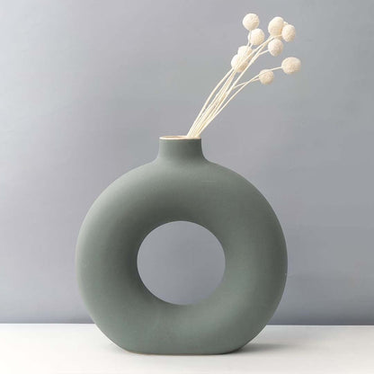 Grey round ceramic vase with hole design styled with white dried flower stems modern home decor accent for table.