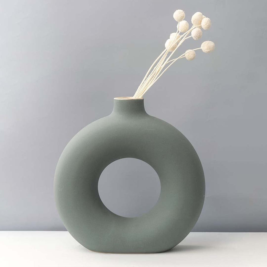 Grey round ceramic vase with hole design styled with white dried flower stems modern home decor accent for table.